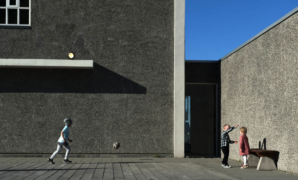 Bambini che giocano a palla contro una parete grigia al sole, centro urbano di Ísafjörður, Islanda nord-occidentale.