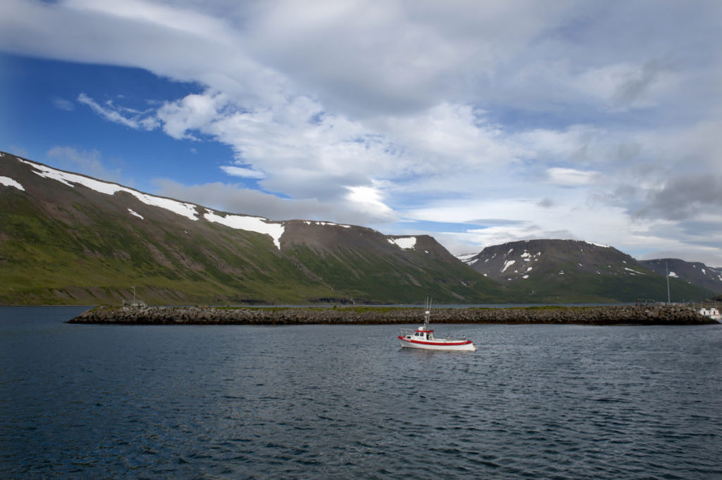 Barca rossa sul fiordo di Ísafjörður, circondata da montagne innevate sotto un cielo nuvoloso, Islanda nord-occidentale.