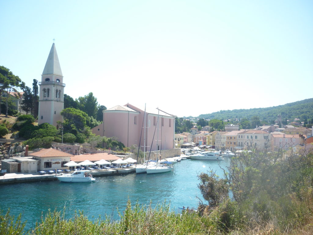 Vista su un piccolo villaggio croato con un campanile a punta, barche bianche e edifici colorati