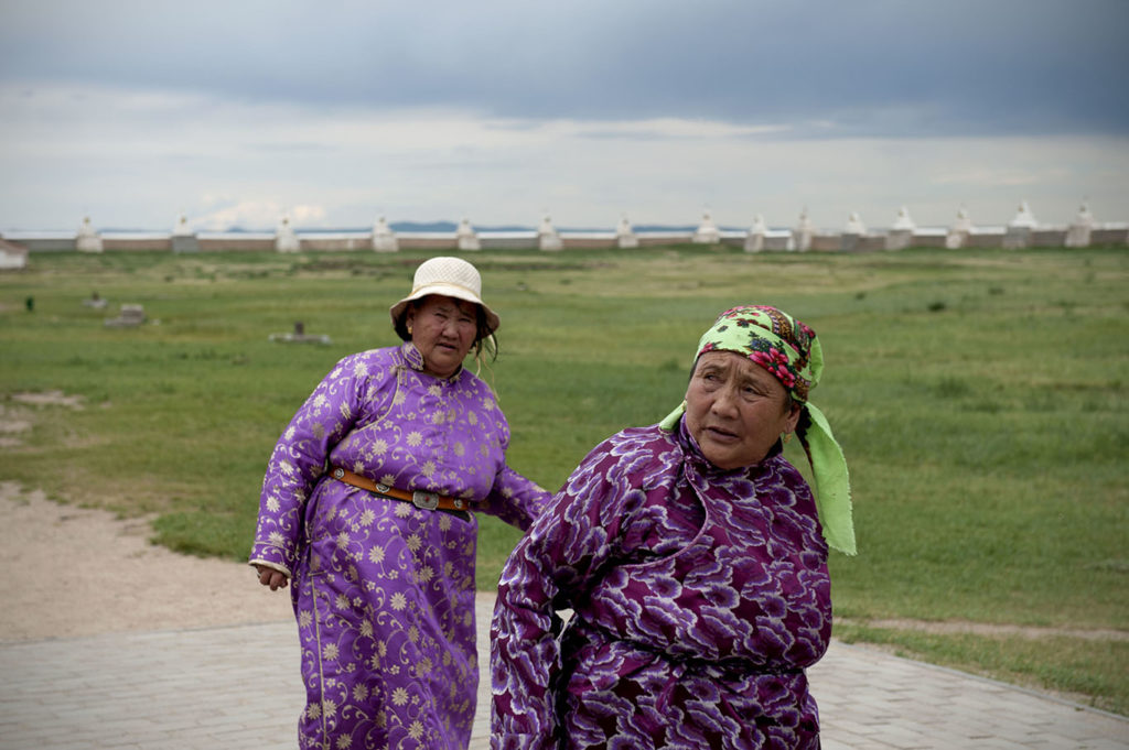 Due donne mongole con abiti tradizionali colorati camminano in una zona rurale, Kharkhorin.
