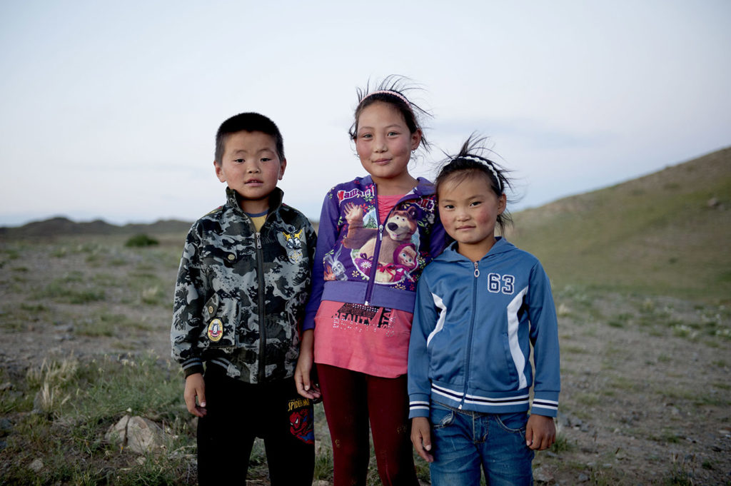 Tre bambini mongoli in posa con abiti casual davanti a un cielo limpido nella steppa
