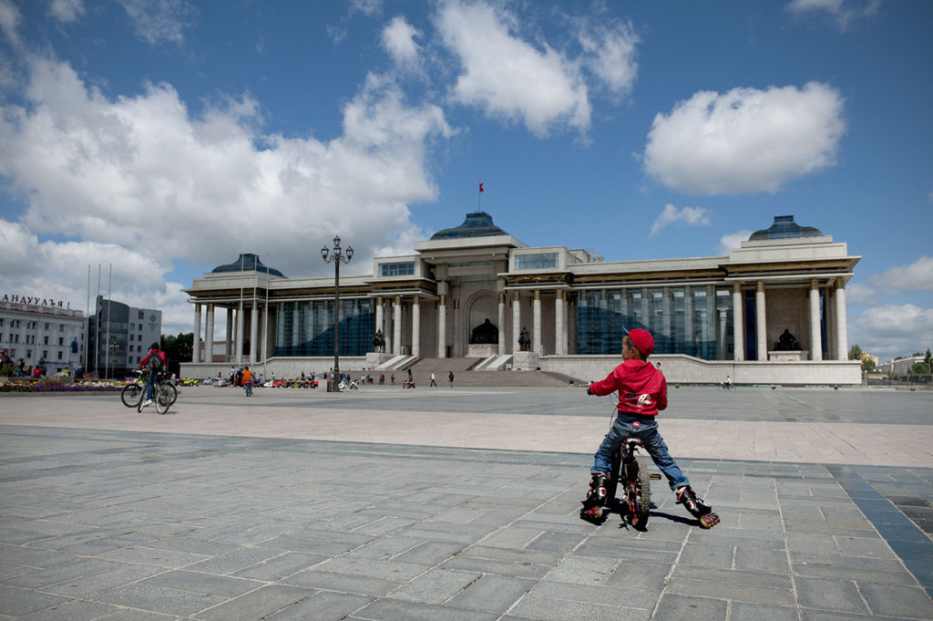 Bambino in bicicletta sulla piazza centrale di Ulan Bator con il Palazzo del Governo sullo sfondo
