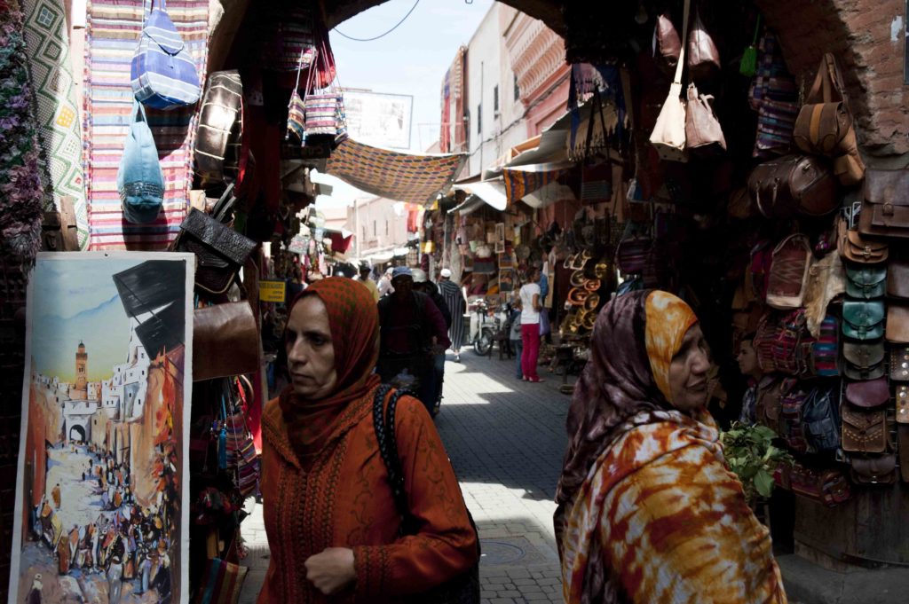 Strada affollata nel souk di Marrakech con donne in abiti tradizionali marocchini.