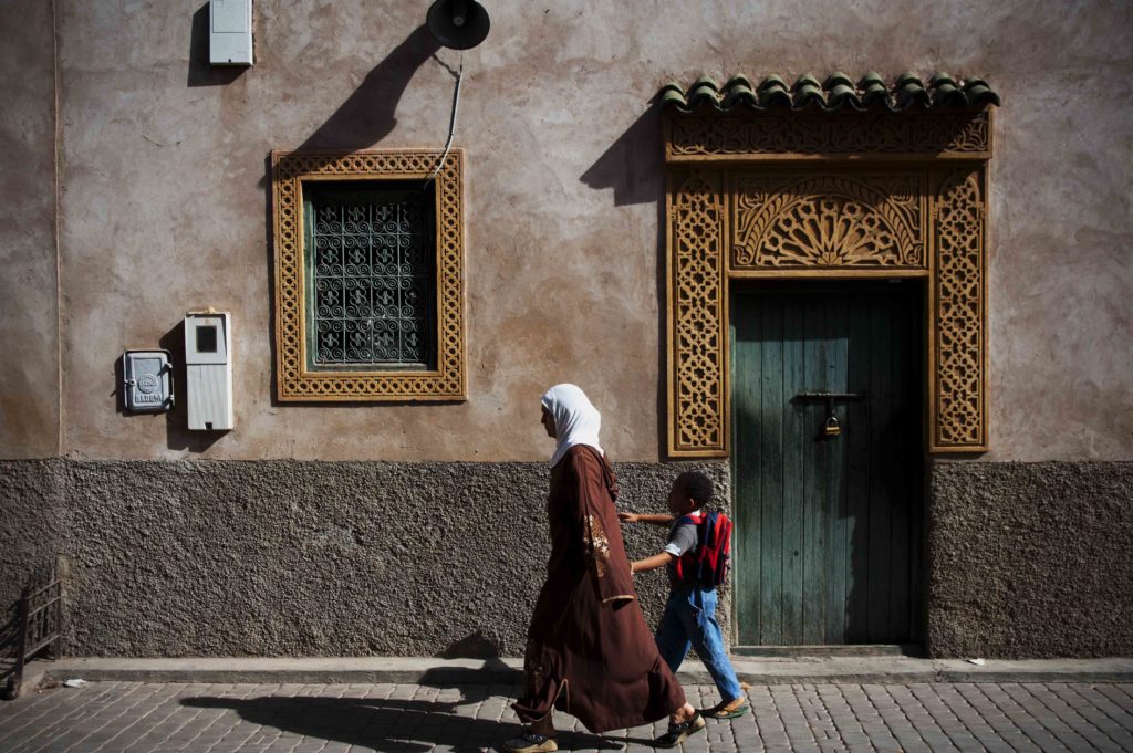 Donna con abito tradizionale e bambino che camminano lungo una strada del centro storico di Marrakech.