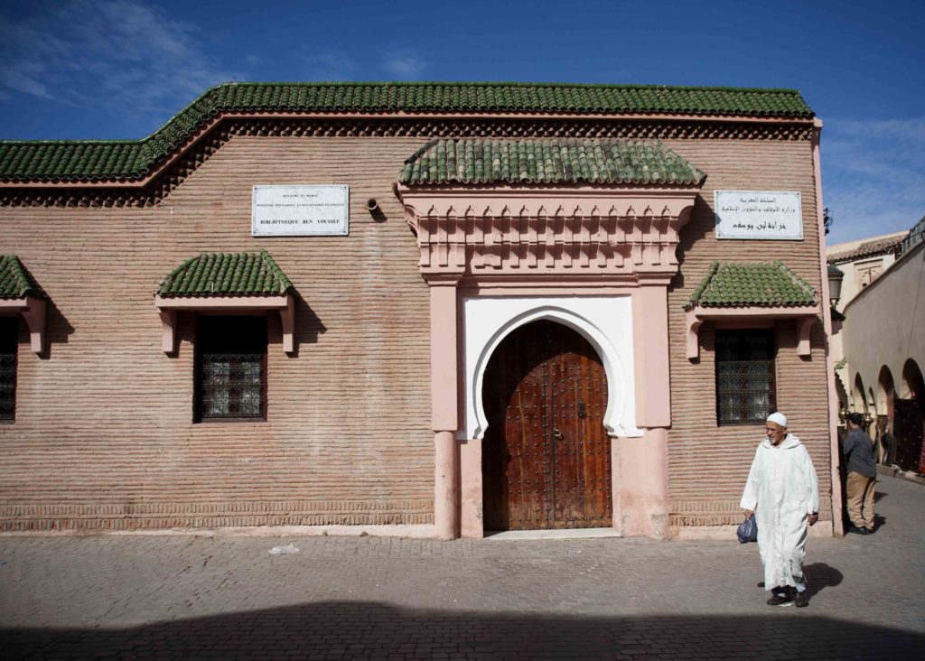 Facciata della storica Medersa Ben Youssef di Marrakech con portale in legno intagliato e architettura tradizionale.