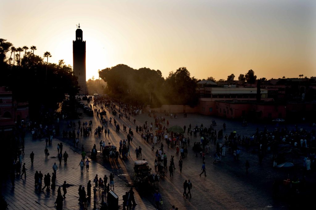 Tramonto sulla piazza Jemaa el-Fna a Marrakech con folla di turisti e minareto della moschea Koutoubia sullo sfondo.