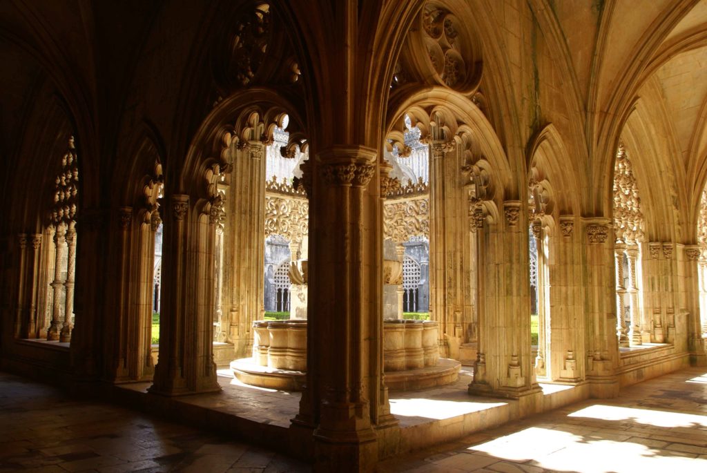 Chiostro gotico con colonne e archi nel Monastero di Batalha, illuminato dalla luce del sole