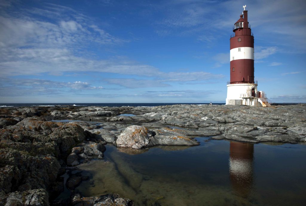 Paesaggio costiero con rocce e faro di Haugjegla, Norvegia, sotto un cielo azzurro.