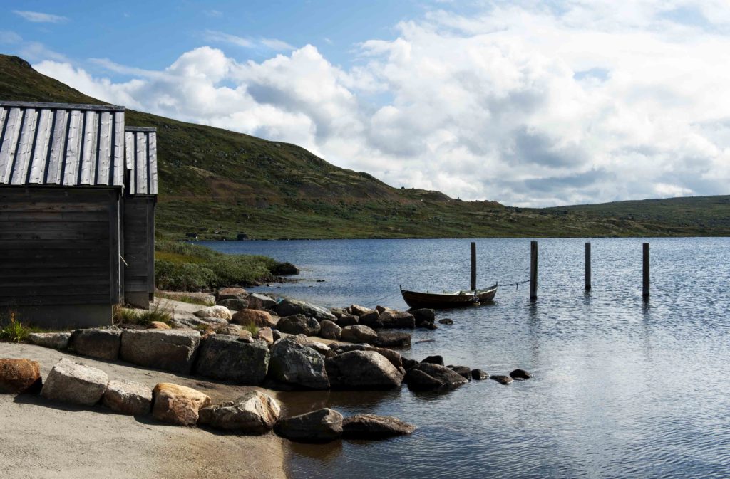 Barca ormeggiata su lago montano con colline verdi e cielo nuvoloso nell'Hardangervidda, Norvegia.