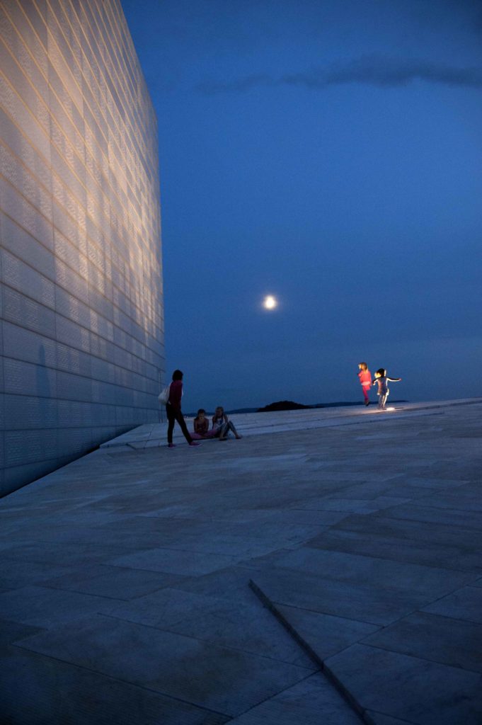 Passeggiata serale sull’Opera House di Oslo con luna piena e cielo blu scuro.