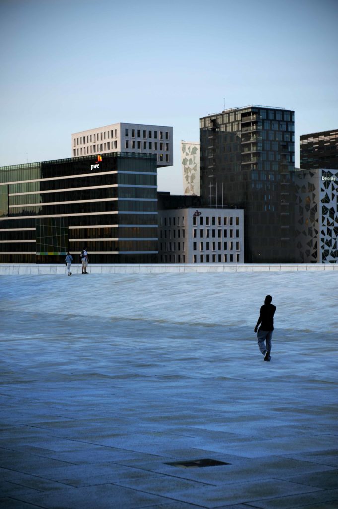 Persona che cammina sulla terrazza del Teatro dell'Opera di Oslo con skyline moderno sullo sfondo.