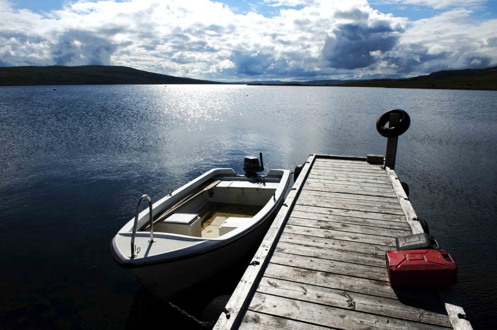 Barca ormeggiata su molo in legno con riflessi sul lago Femund, circondato da natura incontaminata.