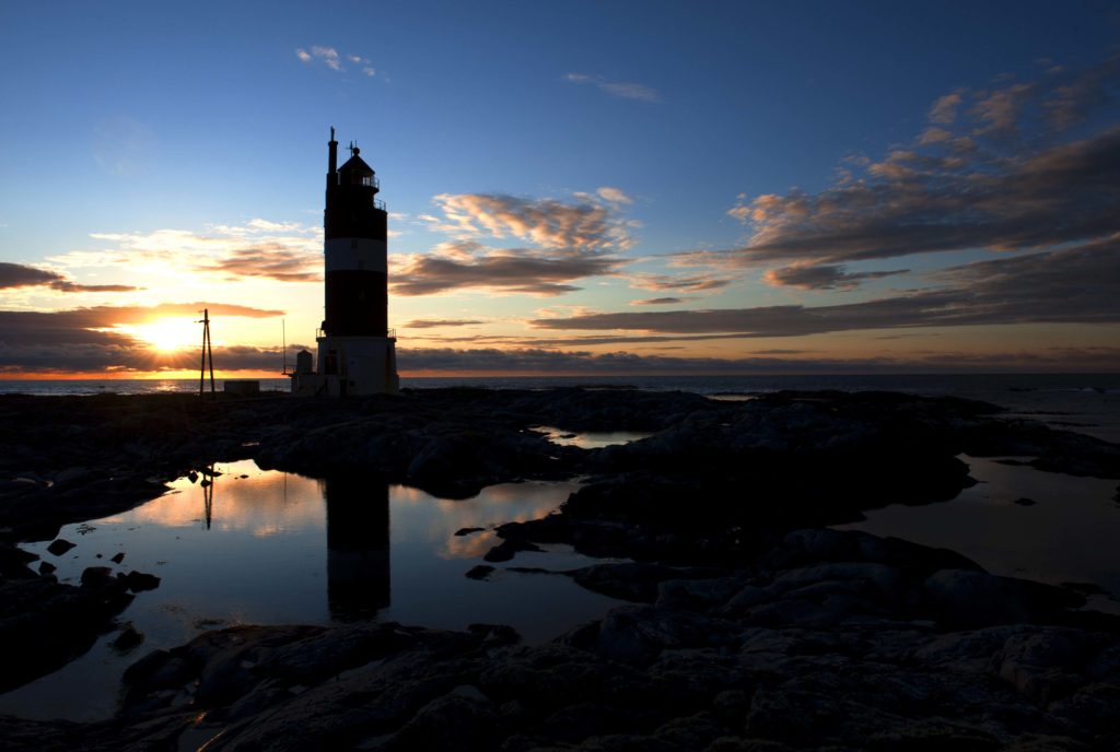 Faro di Haugjegla al tramonto, con cielo colorato e costa rocciosa.