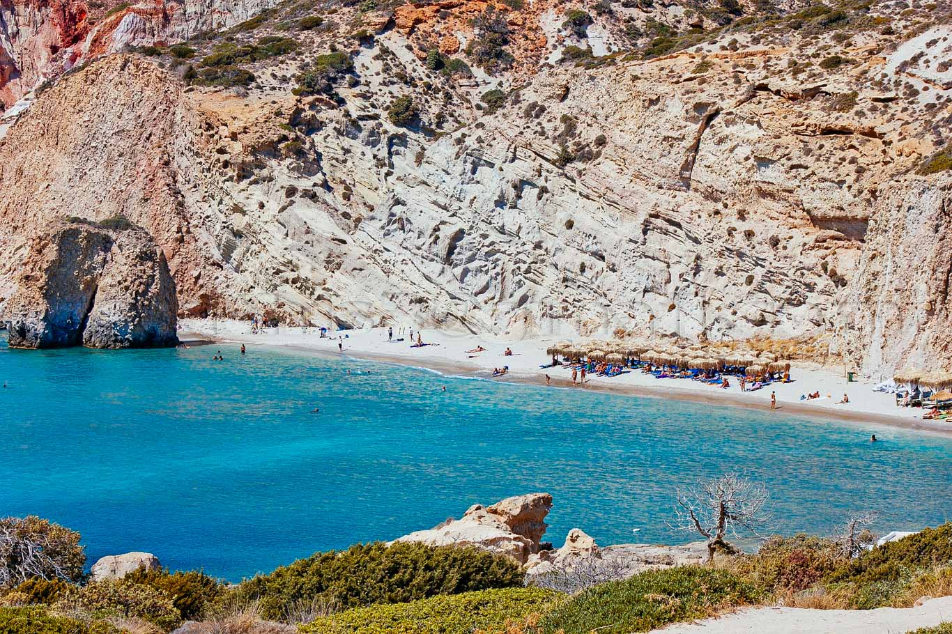 Spiaggia poco affolata con mare blu e pareti di roccia bianca 