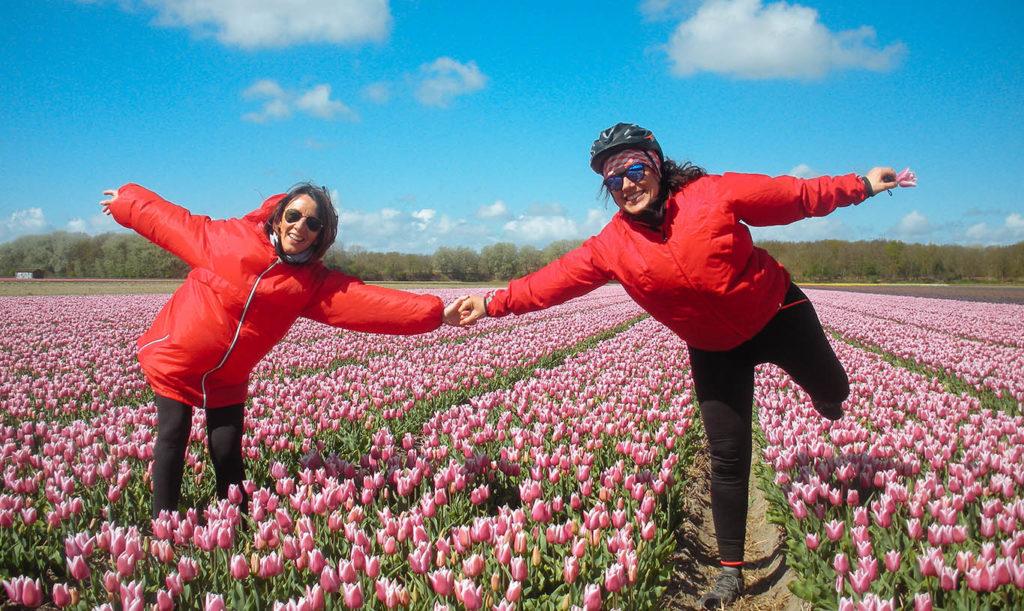 Two happy women both wearing red windbreakers holding hands in a field of pink tulips