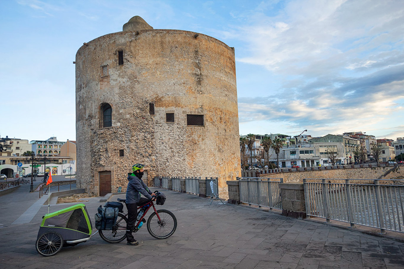 Centro storico di Alghero con Torre Sulis e un cliclista fermo sulla ciclabile lungo la costa