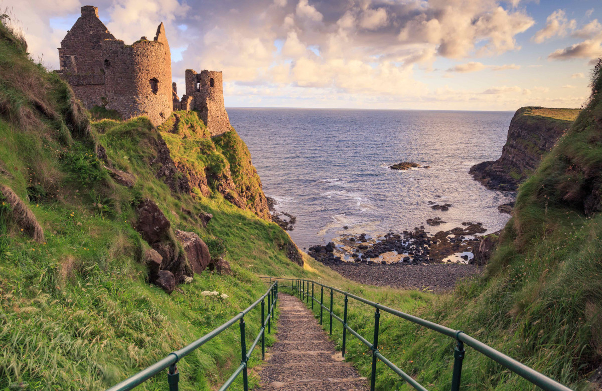 Stradina in discesa con rovine di un castello sullo sfondo verso Downhill Beach