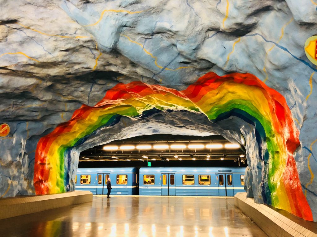 Stazione della metropolitana di Stoccolma, con pareti color arcobaleno e metropolitana blu sullo sfondo