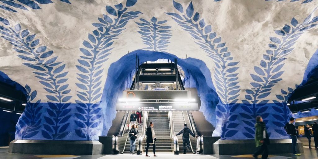 Stazione della metropolitana di Stoccolma, con muri bianchi decorati di blu e scale mobili