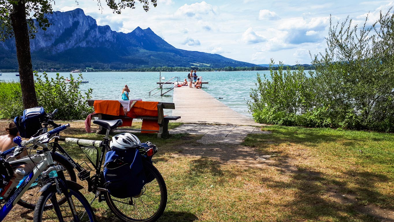 Bici parcheggiate e un molo con montagne sullo sfondo con delle persone che si stanno rilassando