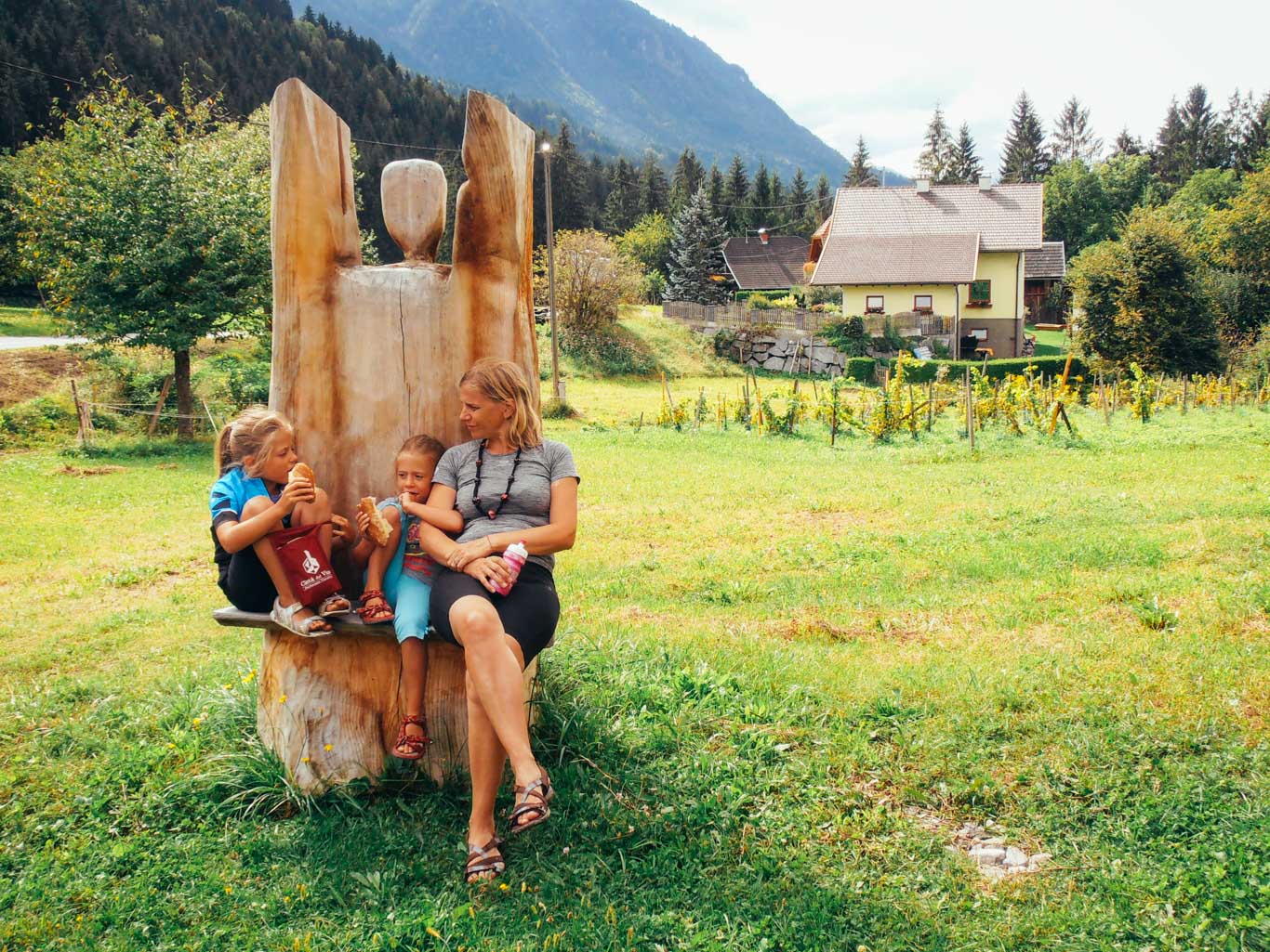 Bambine che mangiano uno snack e si godono una pausa con la mamma in una panchina in legno