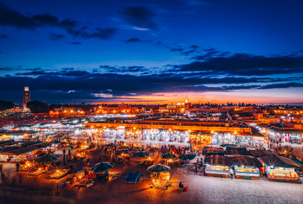 Panorama serale di Jemaa el-Fna con minareto della Moschea Koutoubia, luci del mercato e cielo blu, Marrakech Marocco