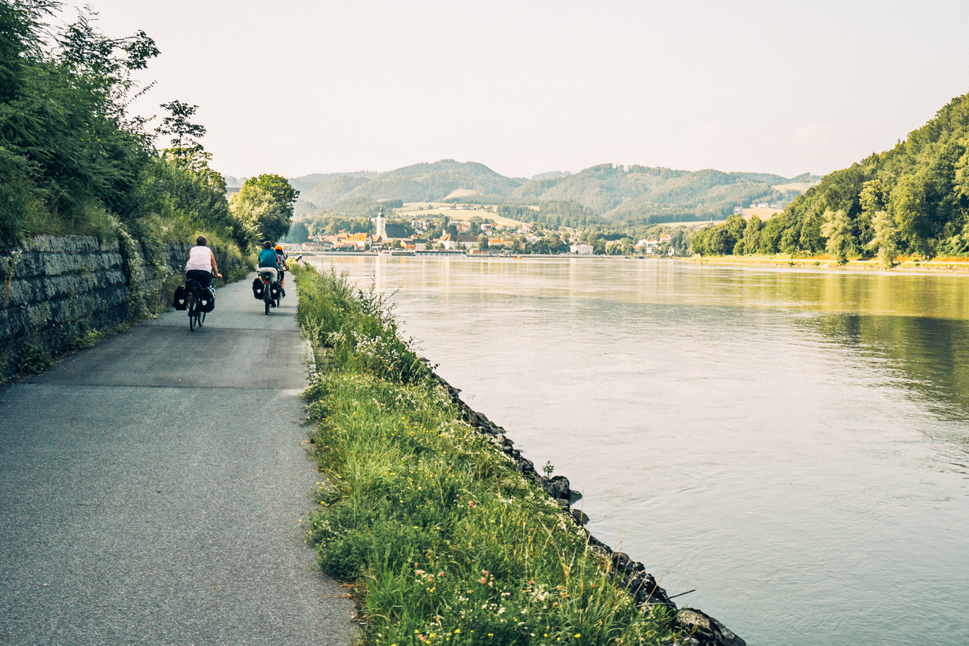 Ciclabile lungo fiume con paesaggio sulle colline e un borgo in lontananza