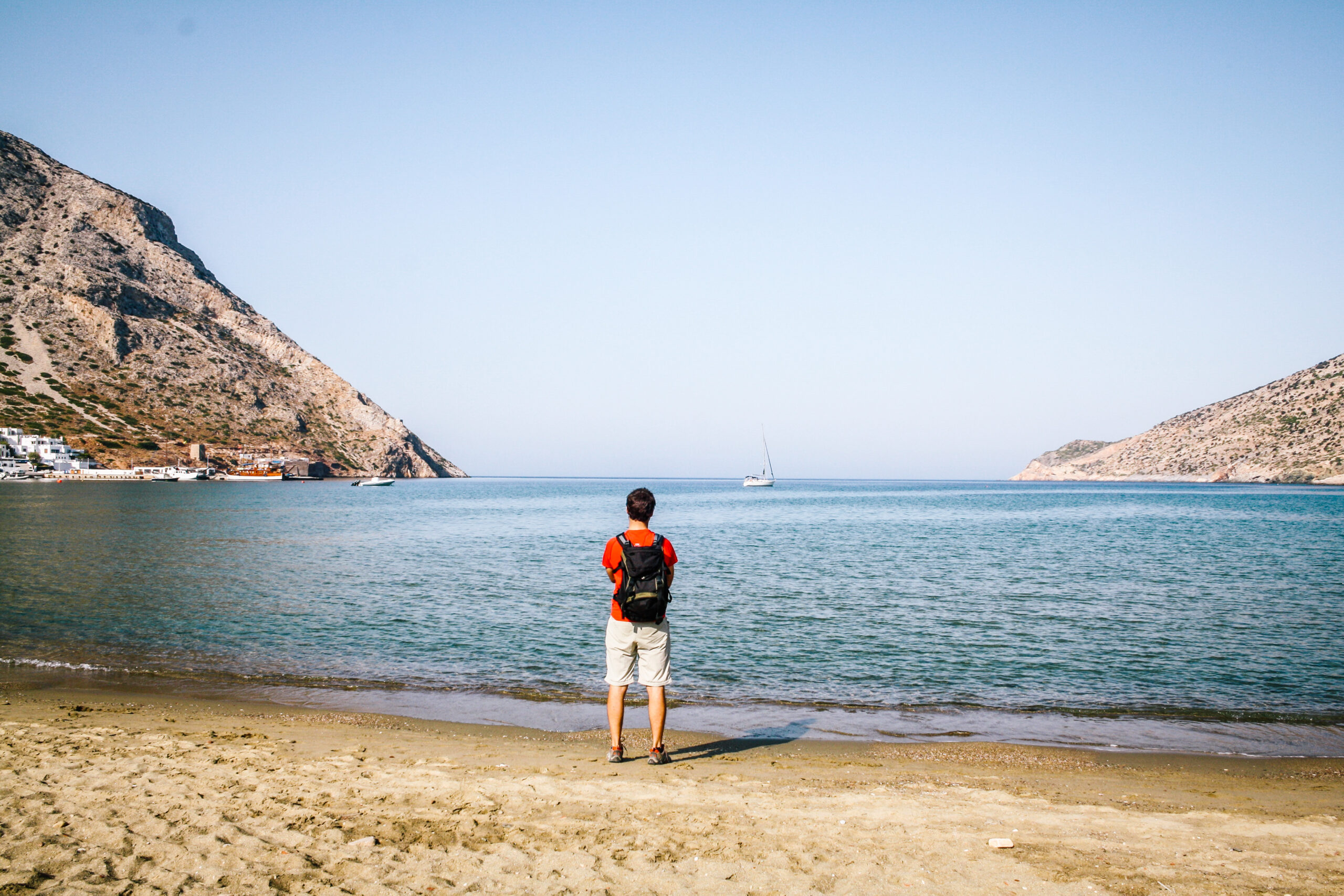 Uomo di spalle con zaino che guarda il mare dalla spiaggia