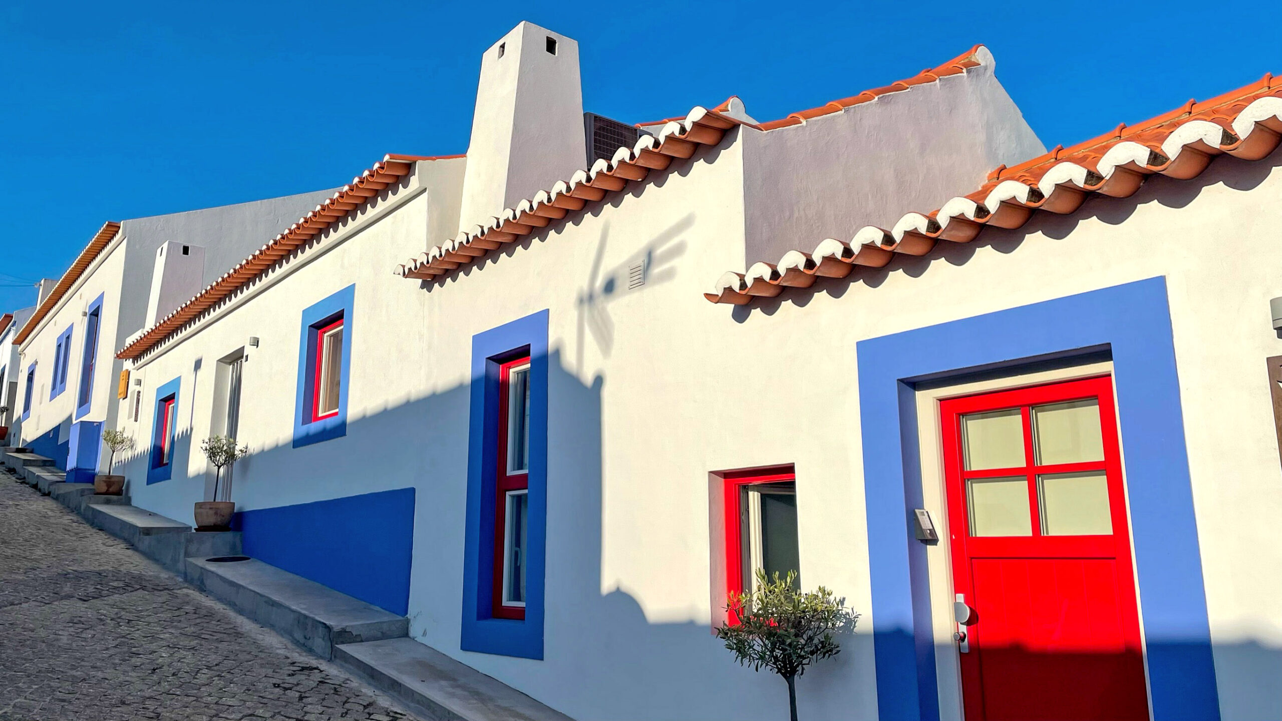 Casette bianche con porte rosse ai lati di una strada a ciottoli in salita in Portogallo