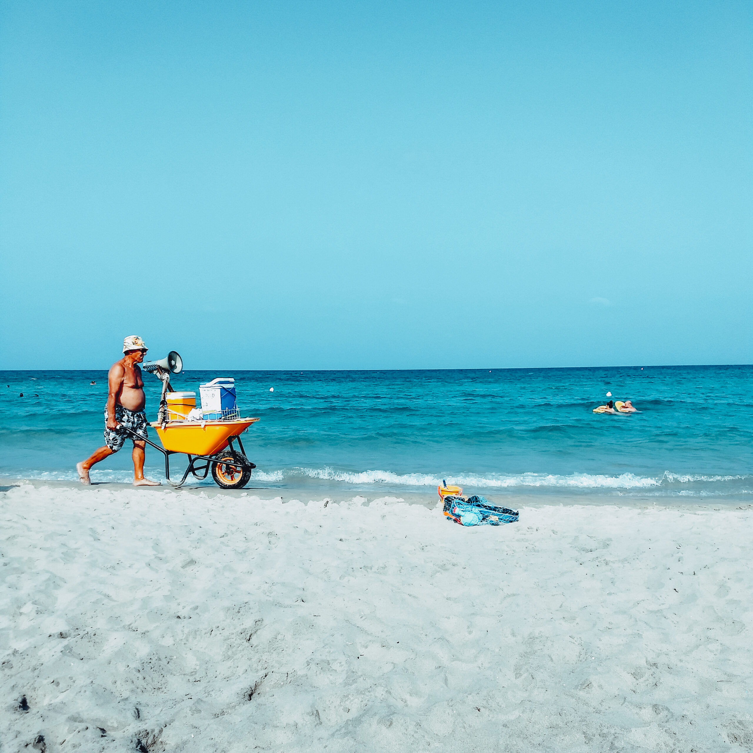 Un signore in costume spinge una carriola gialla in riva al mare