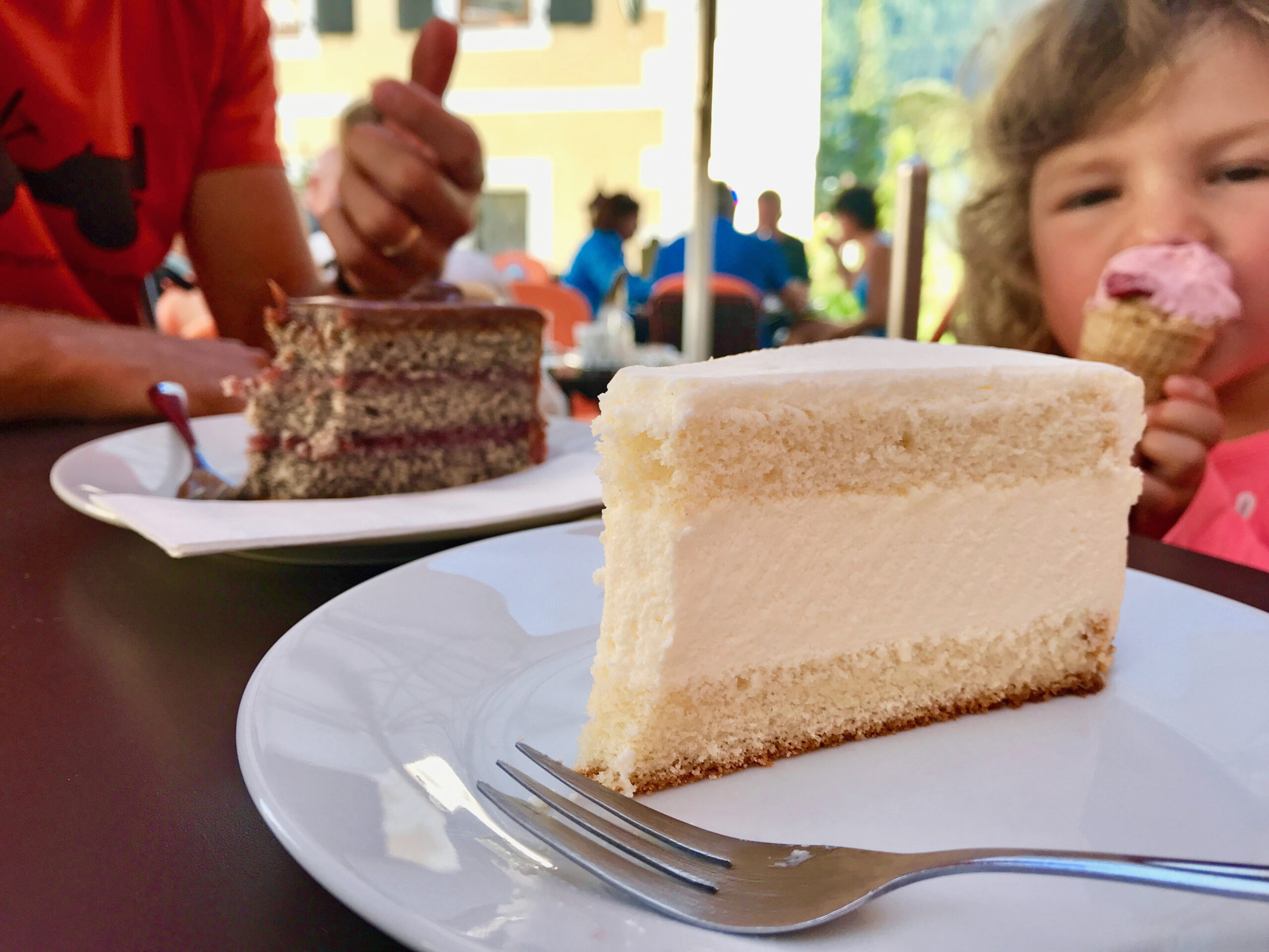 Dettaglio di due fette di torte con crema e marmellata e sullo sfondo una bambina che mangia un gelato