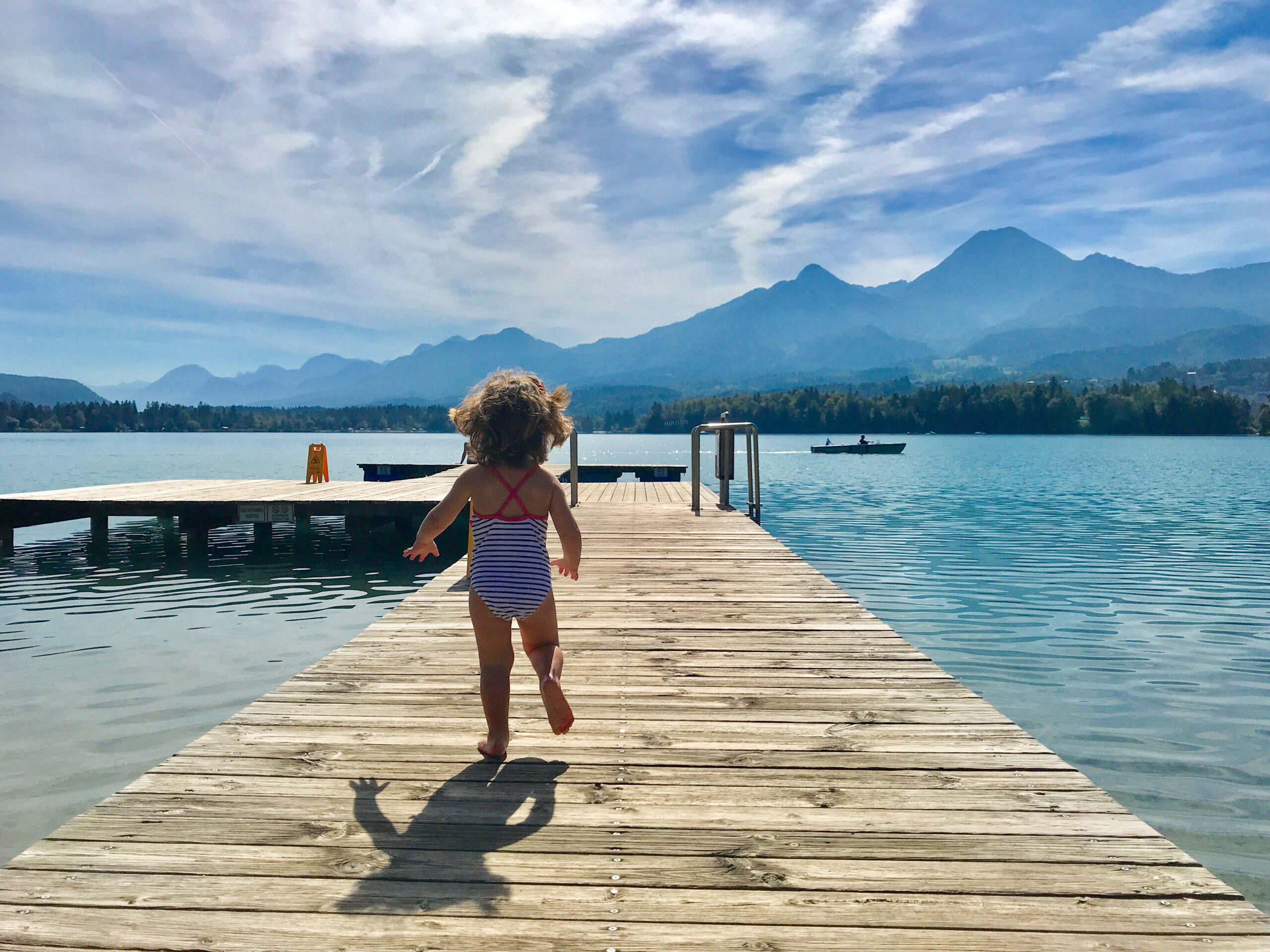 Una bambina che corre di spalle sulla pedana di legno di un lago