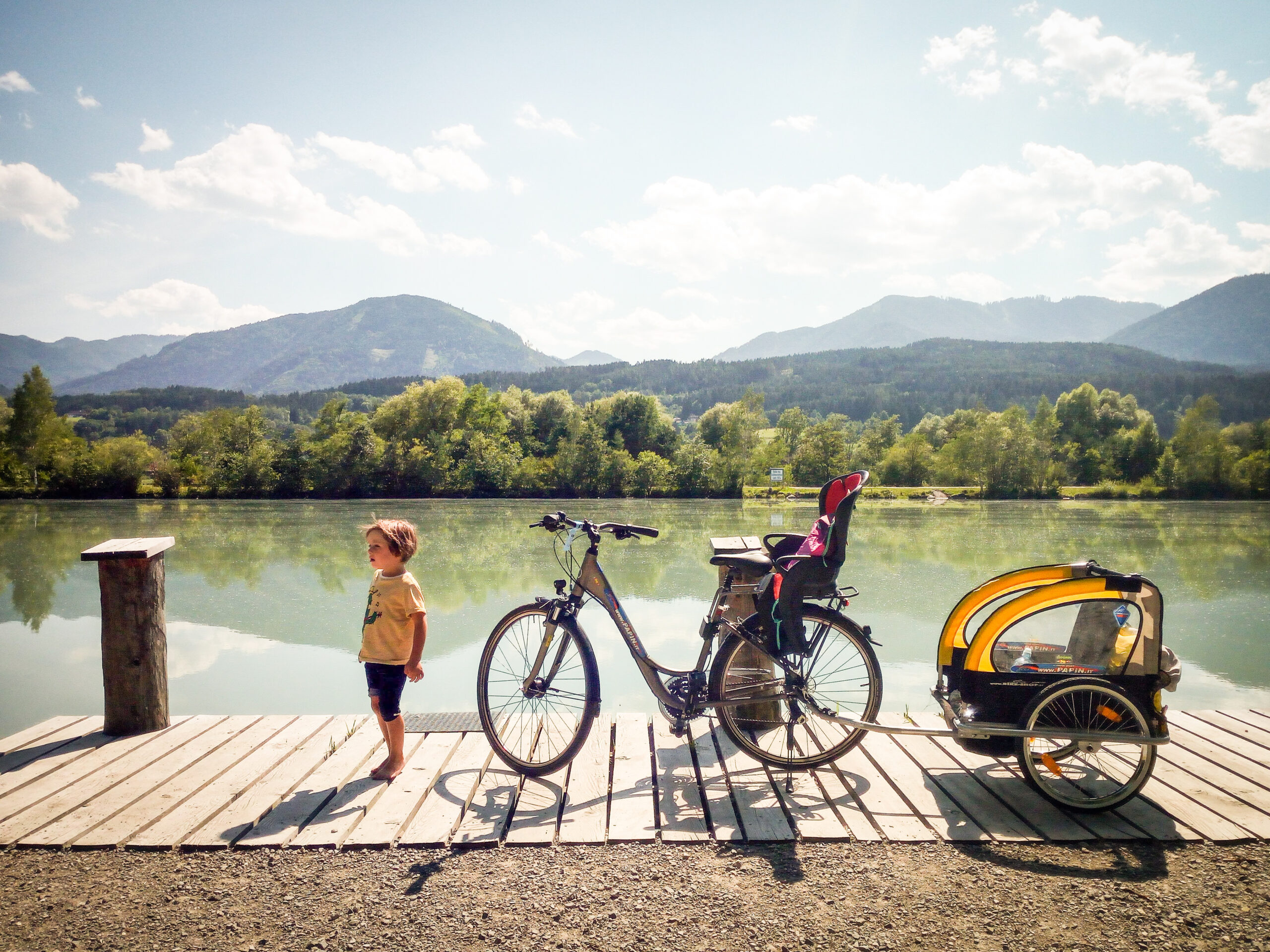 Bici con carrellino ferma davanti ad un lago e un bambino scalzo al suo fianco