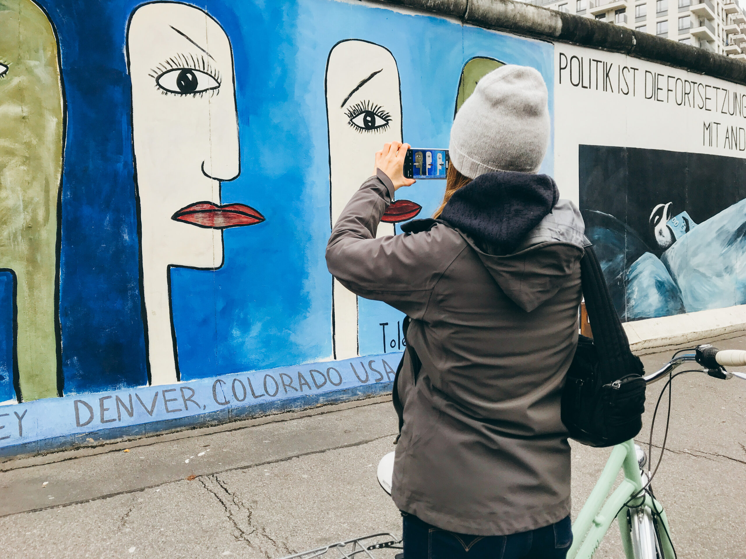 Murales su sfondo blu raffigurante volti con un solo occhio e una bocca nella East Side Gallery, Berlino