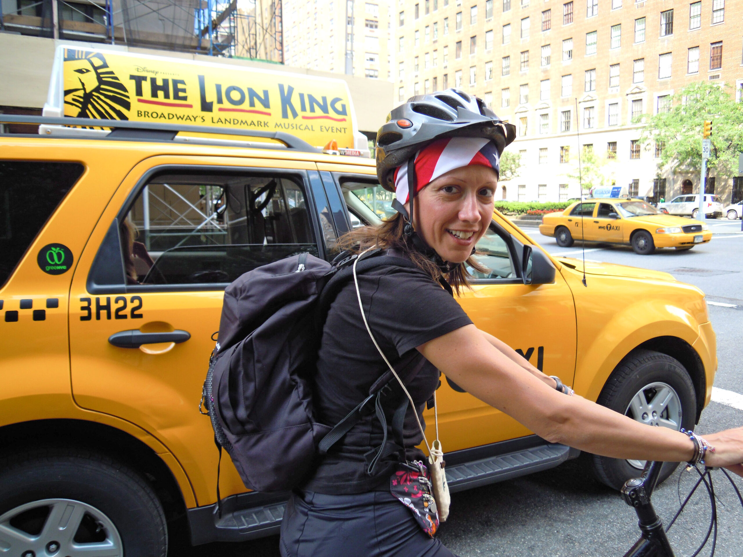 Donna in bicicletta e taxi giallo dietro di lei