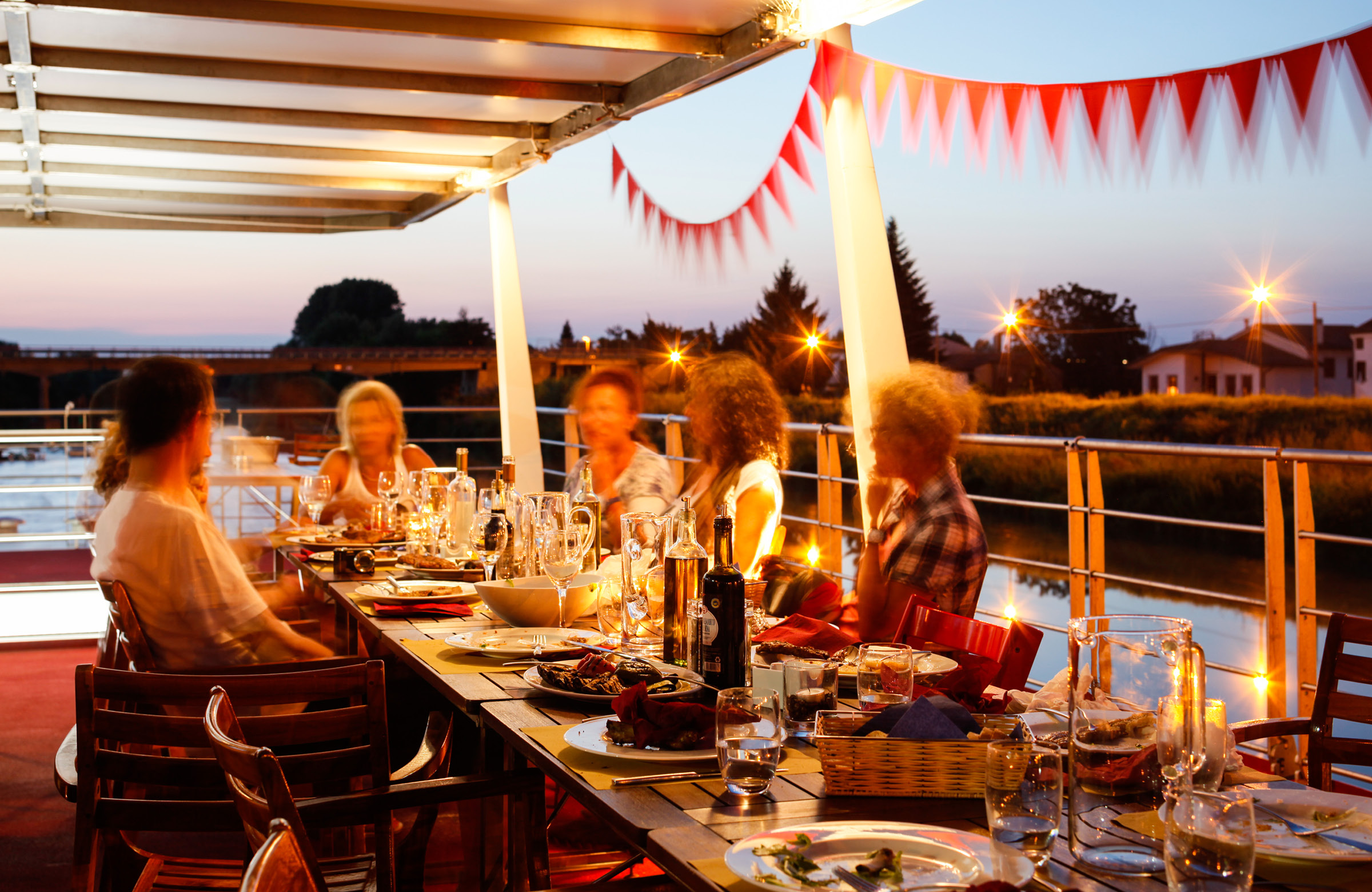 People chatting in front of a set table in the sun deck of an evening boat