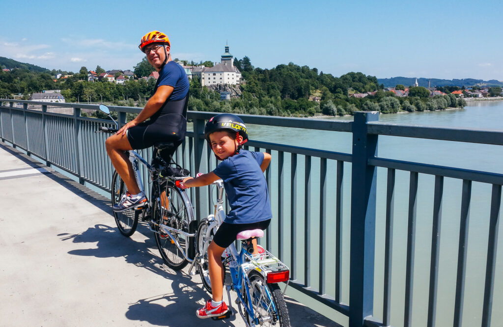 Bambino e papà in bicicletta e nello sfondo un lago della Carinzia