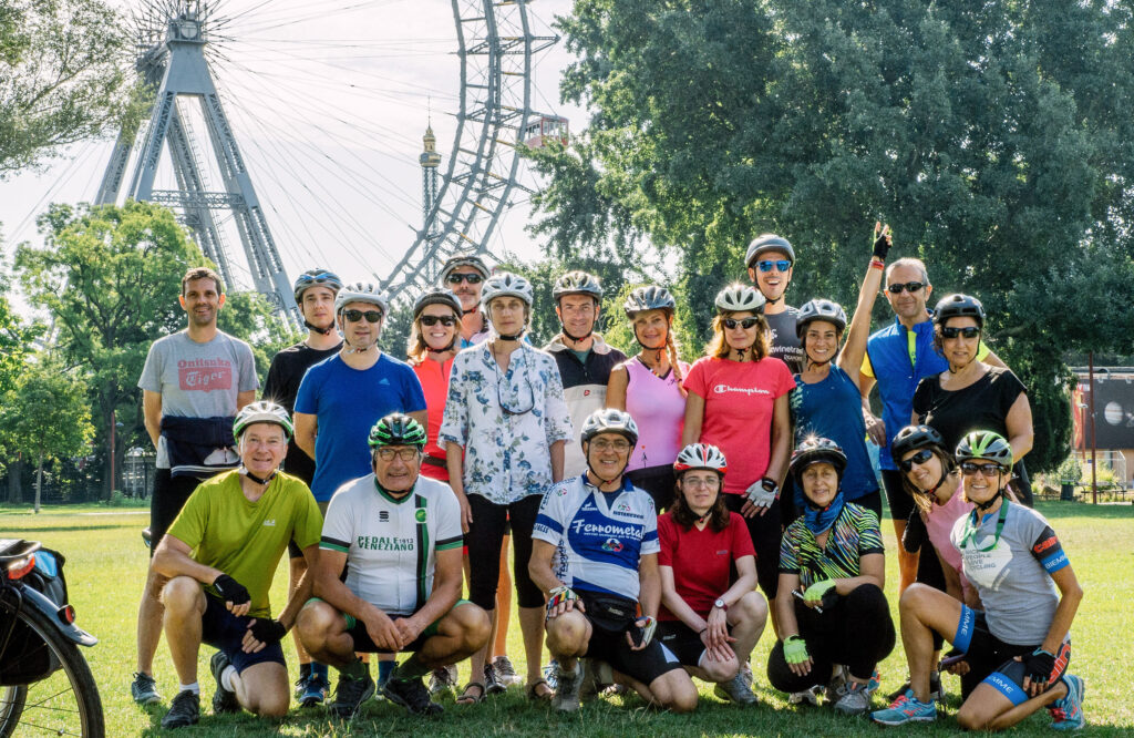 Gruppo di ciclisti viaggiatori con caschetto e dietro una grande  ruota panoramica