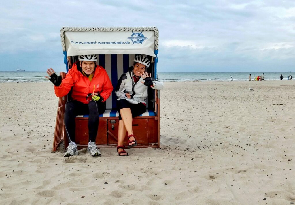 Two cyclists smile and wave at the lens during a break along the Berlin Copenhagen bike path