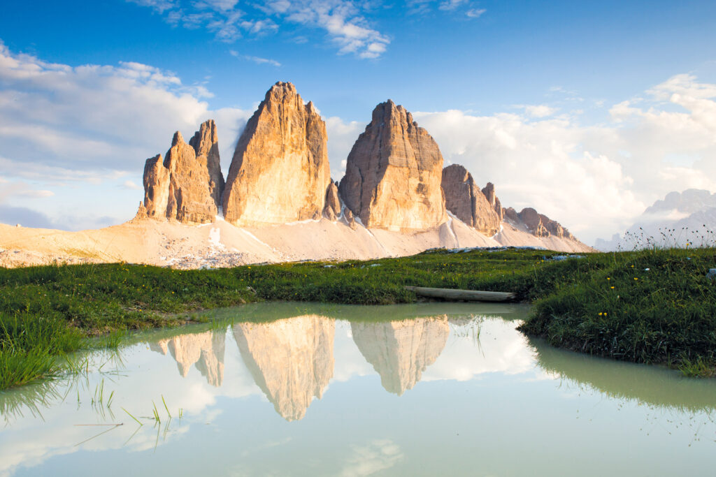 Three peaks of Lavaredo reflected in the clear water of the Adige River, grassy scrubland, eco-sustainable tourism, South Tyrol