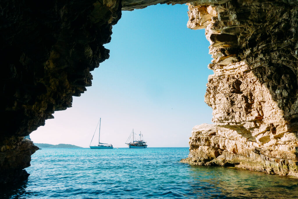 View through a sea cave arch of turquoise water with sailboats, Greek islands bike and barge