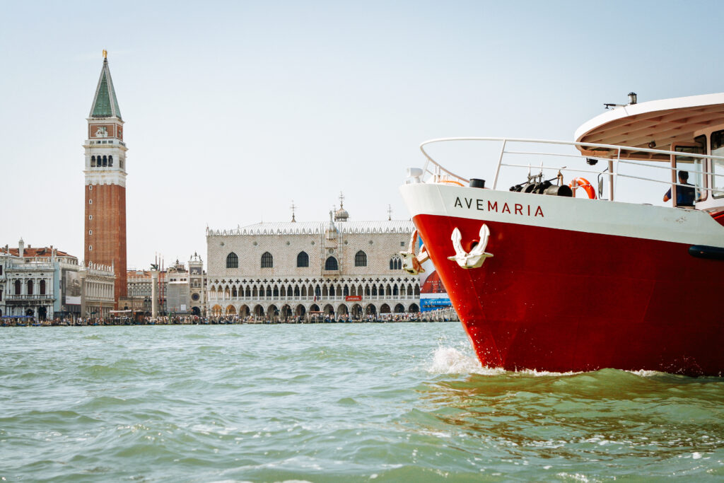 Red boat Ave Maria sailing near St Mark's Square and Doge's Palace, Venice