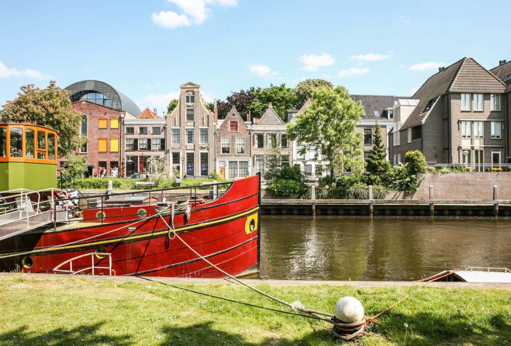 Red barge moored along a Dutch canal with traditional gabled houses, bike and barge tour in the Netherlands