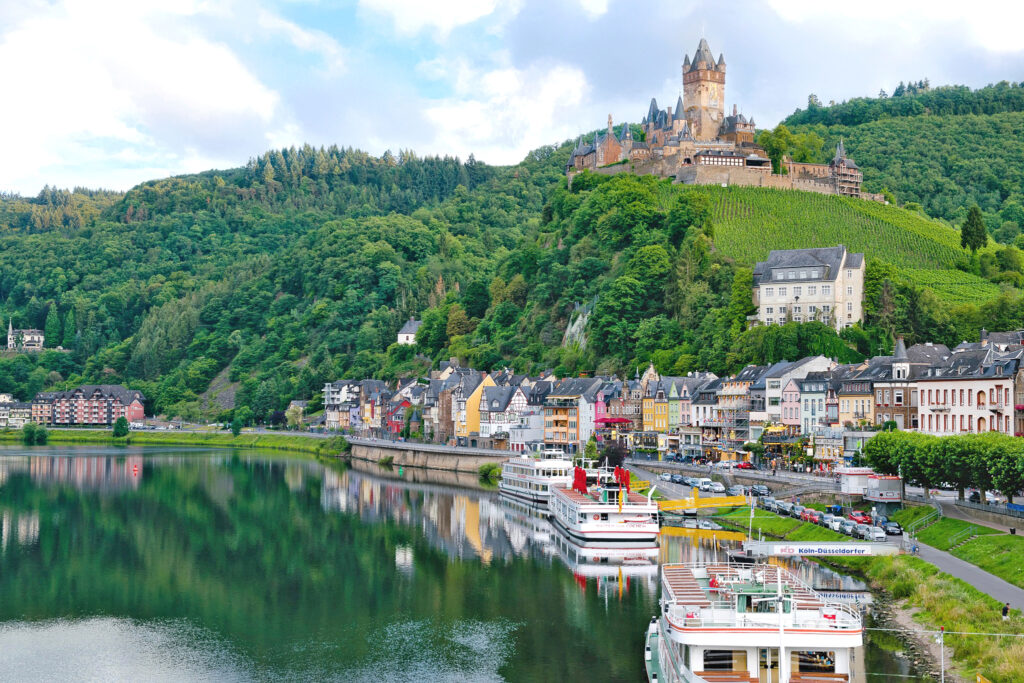 Cochem castle on a wooded hilltop above the Moselle river with boats moored below, Germany cycling route